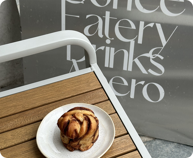 Cinnamon roll served on the terrace with Kosto branding in the background.