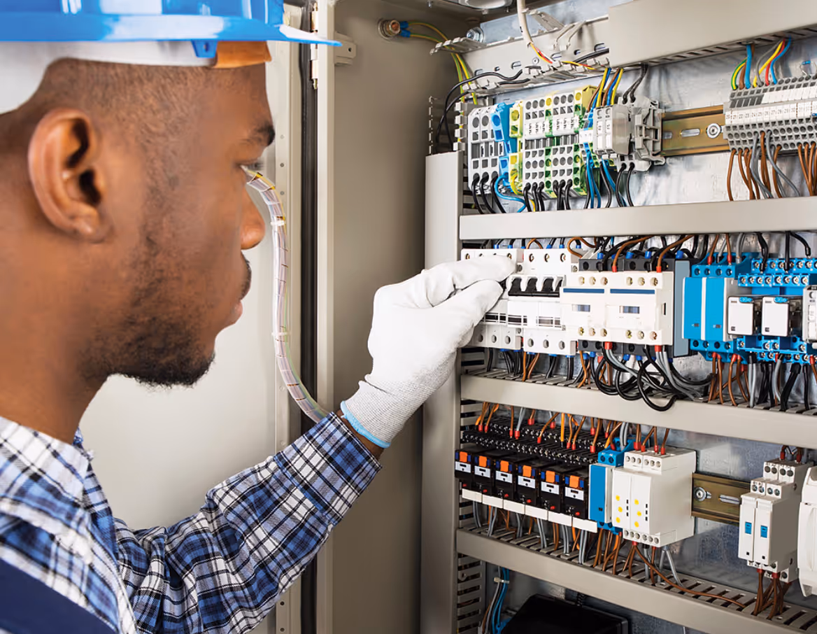 Electrician wearing a blue helmet and gloves adjusting circuit breakers inside an electrical panel.