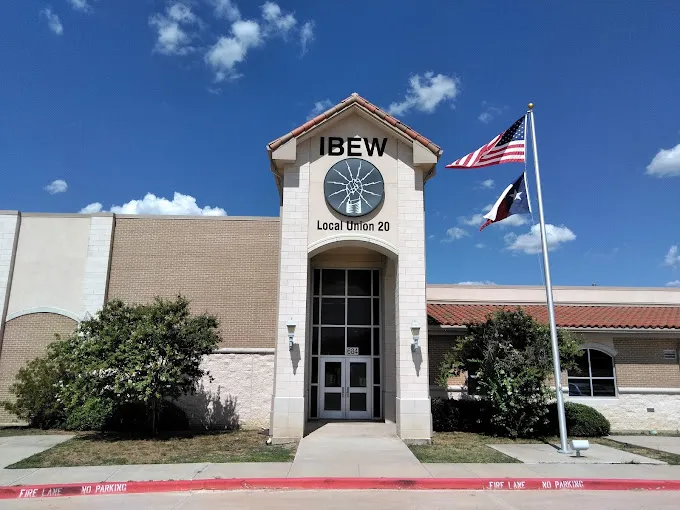 Front view of the IBEW Local Union 20 building with an American flag and a Texas state flag flying on a pole beside the entrance.
