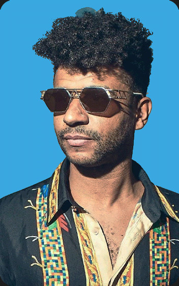 Portrait of DJ Jamie Jones wearing sunglasses and a patterned shirt, set against a blue background