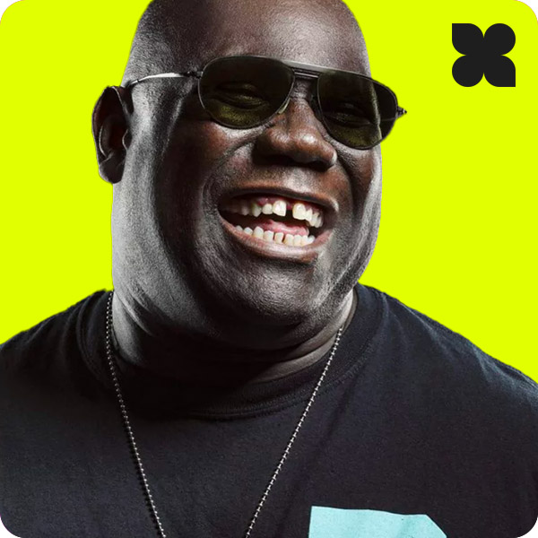 Portrait of DJ Carl Cox wearing sunglasses and a black t-shirt, smiling against a bright yellow background