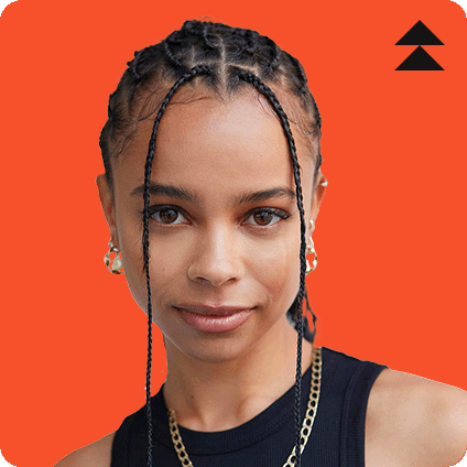 Portrait of DJ TSHA wearing a black top, gold jewelry, and braided hairstyle, set against an orange background