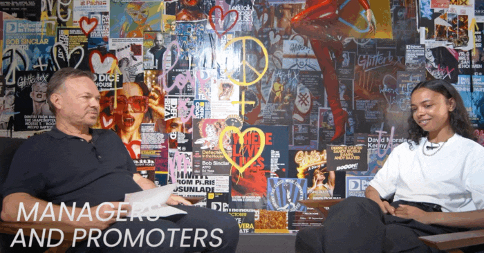 Pete Tong interviewing a music industry professional in front of a vibrant collage wall with music event posters. The text 'Managers and Promoters' appears on the screen