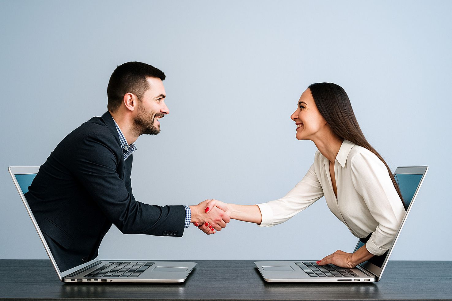 Business professionals smiling and shaking hands through laptop screens, symbolizing virtual partnership and remote collaboration.