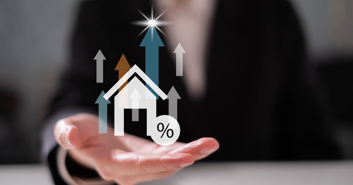 A person in a dark suit presents a floating graphic of a house, arrows, and a percent symbol above one hand.