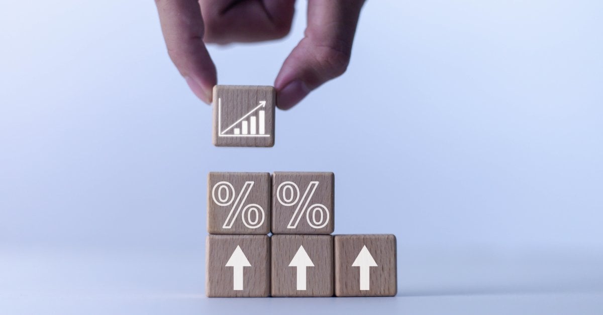 A hand placing a wooden block with a bar graph symbol above stacked cubes marked with percent signs and arrows.