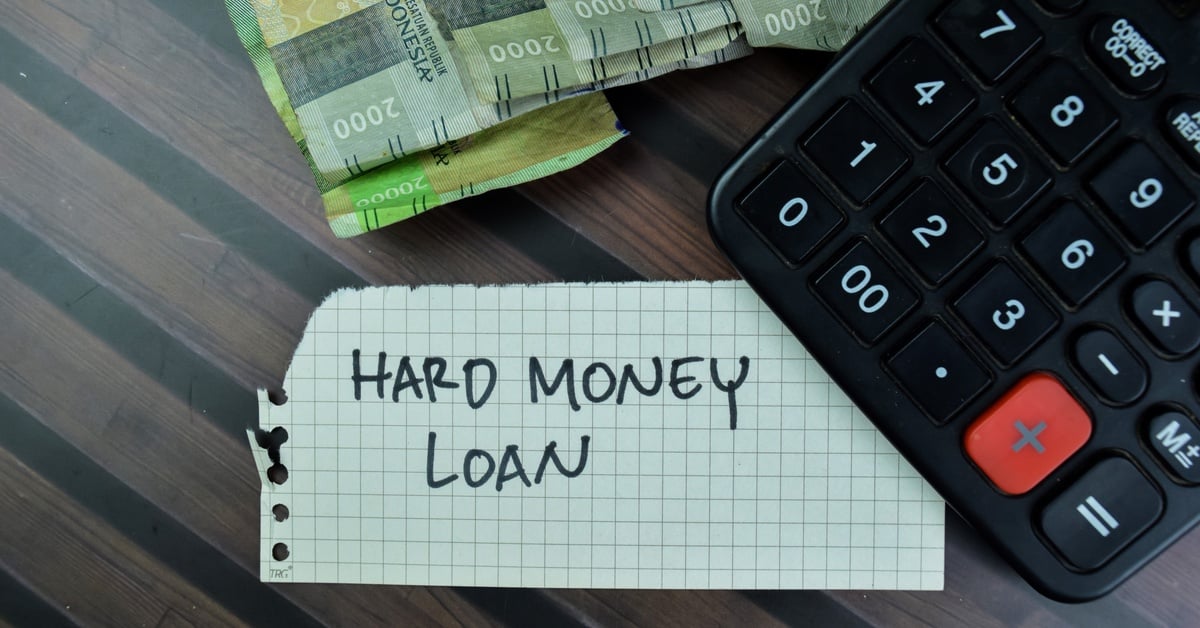 A ripped piece of notebook paper reading “Hard Money Loan” and resting on a table next to a stack of cash and a calculator.