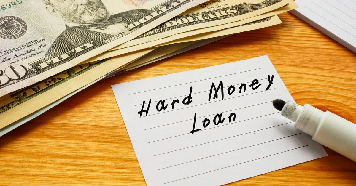 A note card with the words “Hard Money Loan” written on it, sitting on a desk next to a stack of US dollar bills.