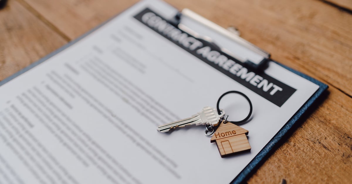 A close-up of a contract agreement on a clipboard. A keyring with a home-shaped keychain rests on the contract.