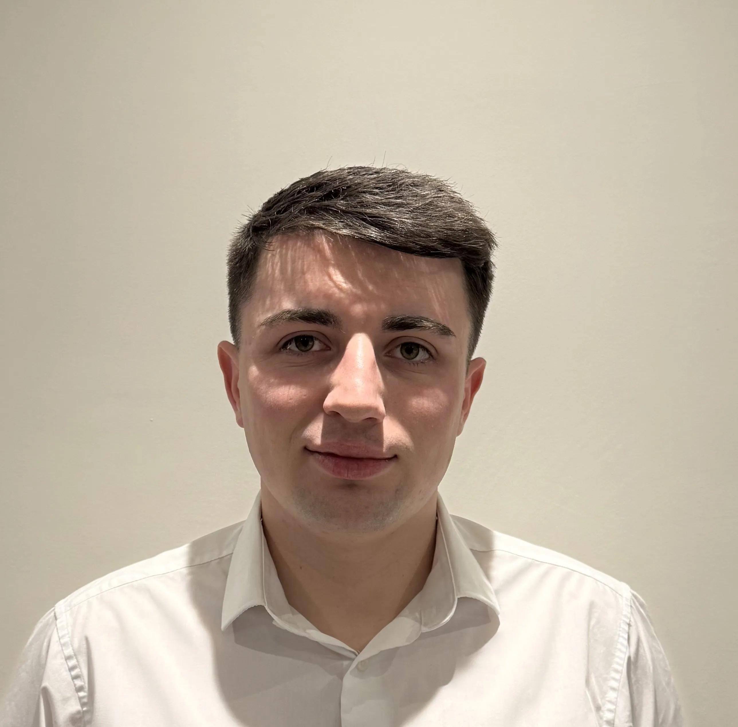 Young man with short dark hair wearing a white collared shirt against a plain light background.