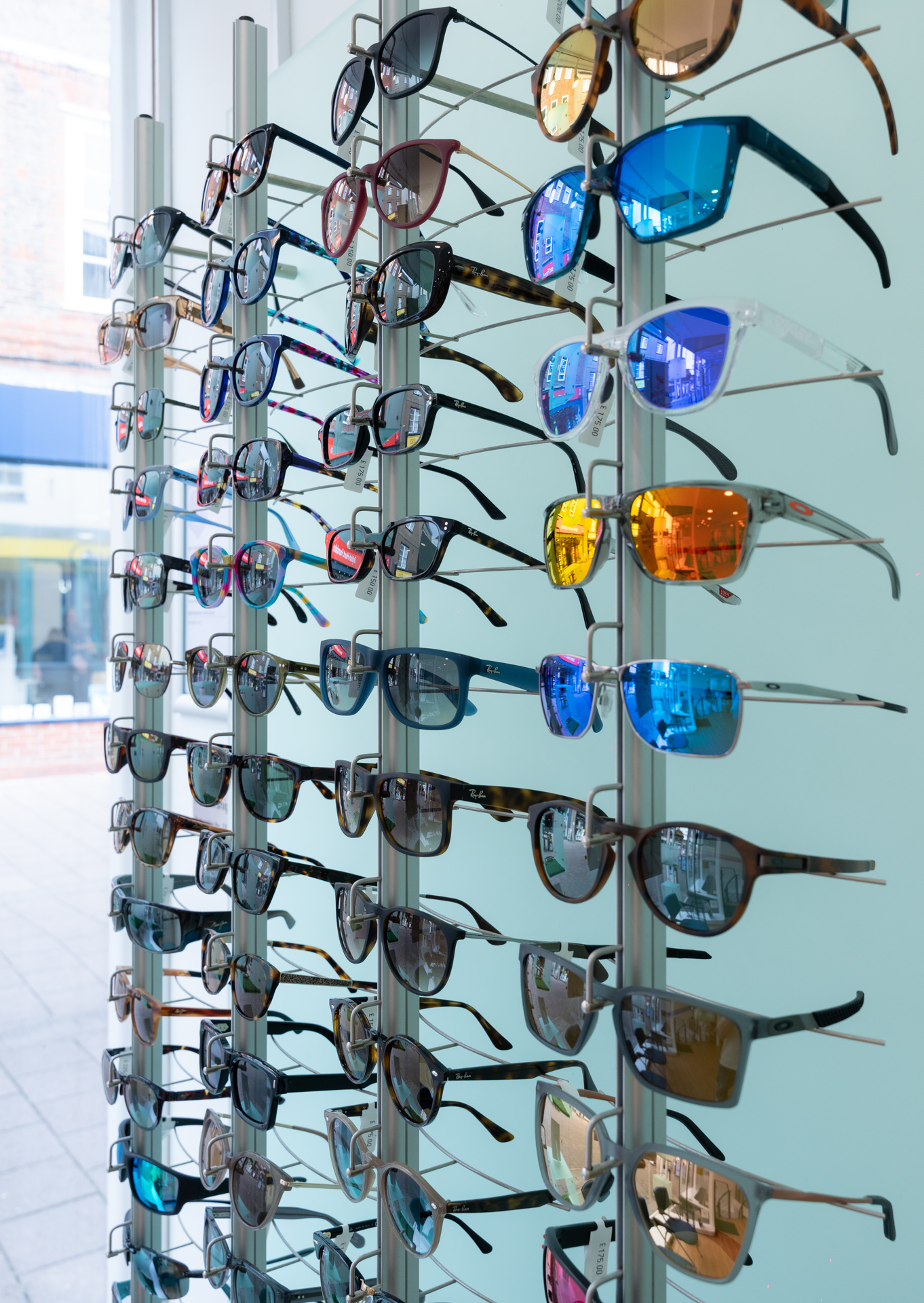 Display rack filled with various sunglasses featuring colorful and reflective lenses in a store window.
