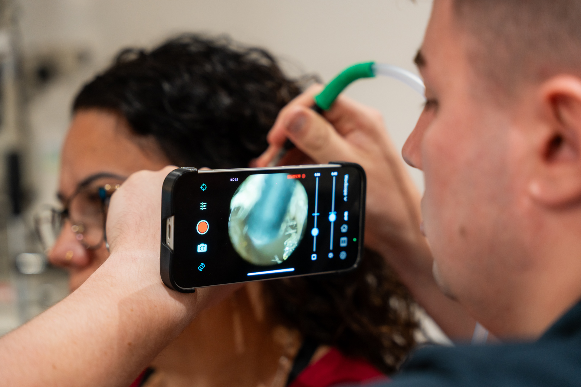 Audiologist using a smartphone and otoscope to examine a woman’s ear with a close-up view on the phone screen.