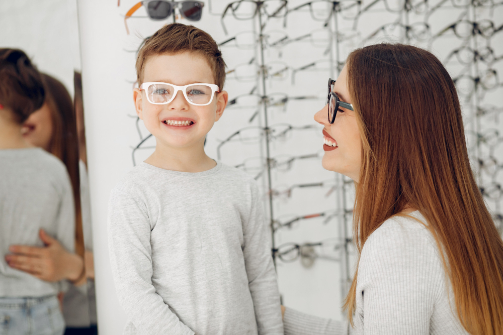 Smiling boy wearing white glasses with a woman in black glasses at an eyewear store.