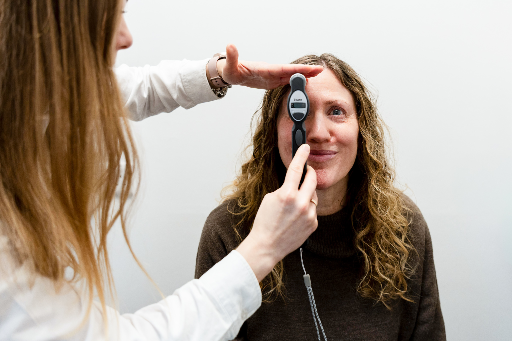 Optician holding a device measuring intraocular pressure on a smiling woman's eye.