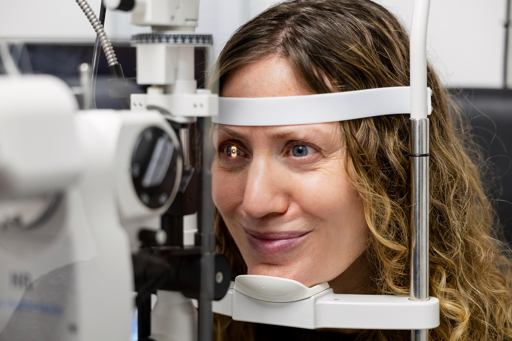Woman with curly hair undergoing an eye exam using a slit lamp machine.