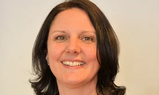 Smiling woman with shoulder-length dark hair and brown eyes against a plain background.