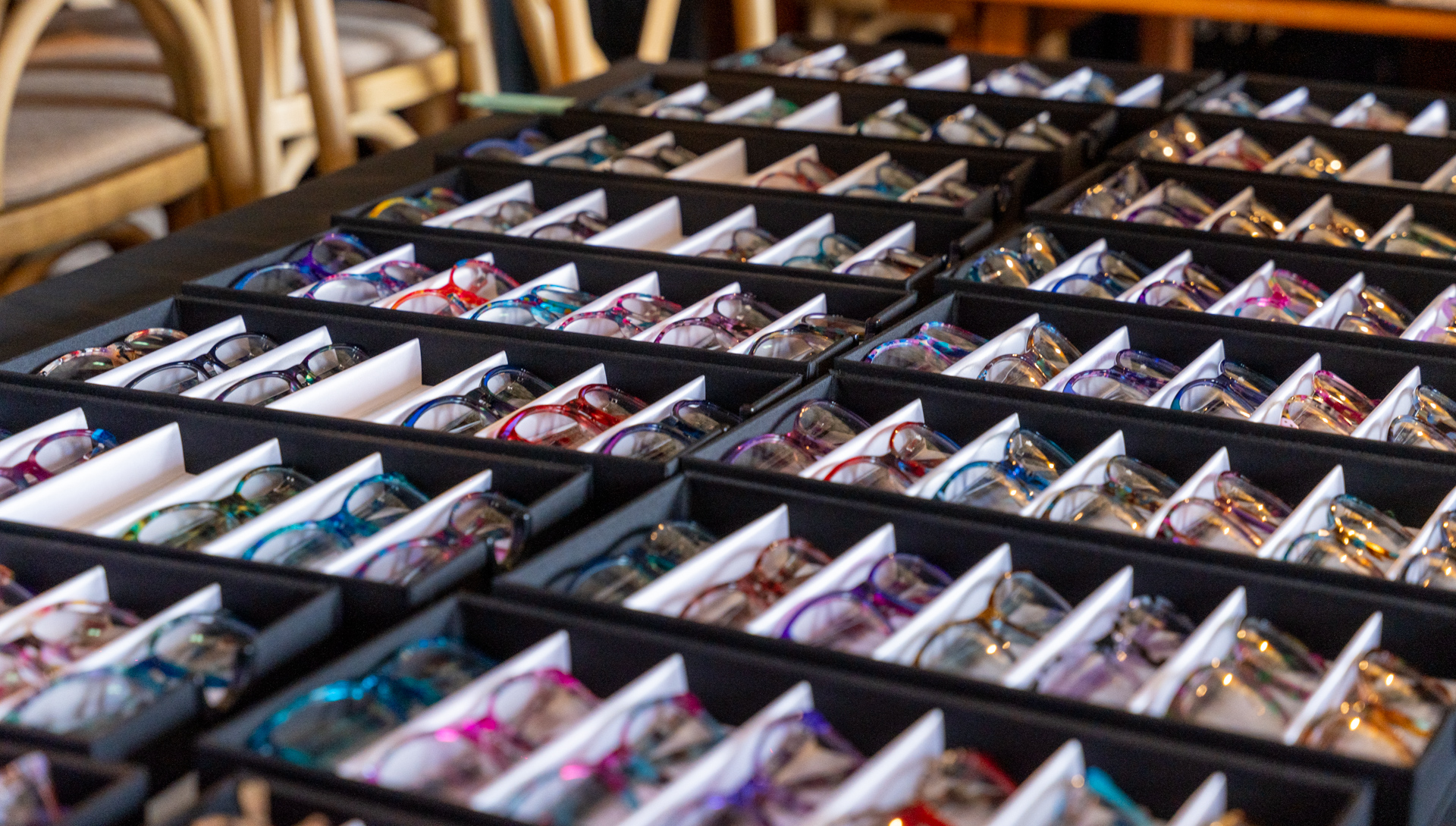 Rows of eyeglasses with colorful frames displayed in organized trays on a table.