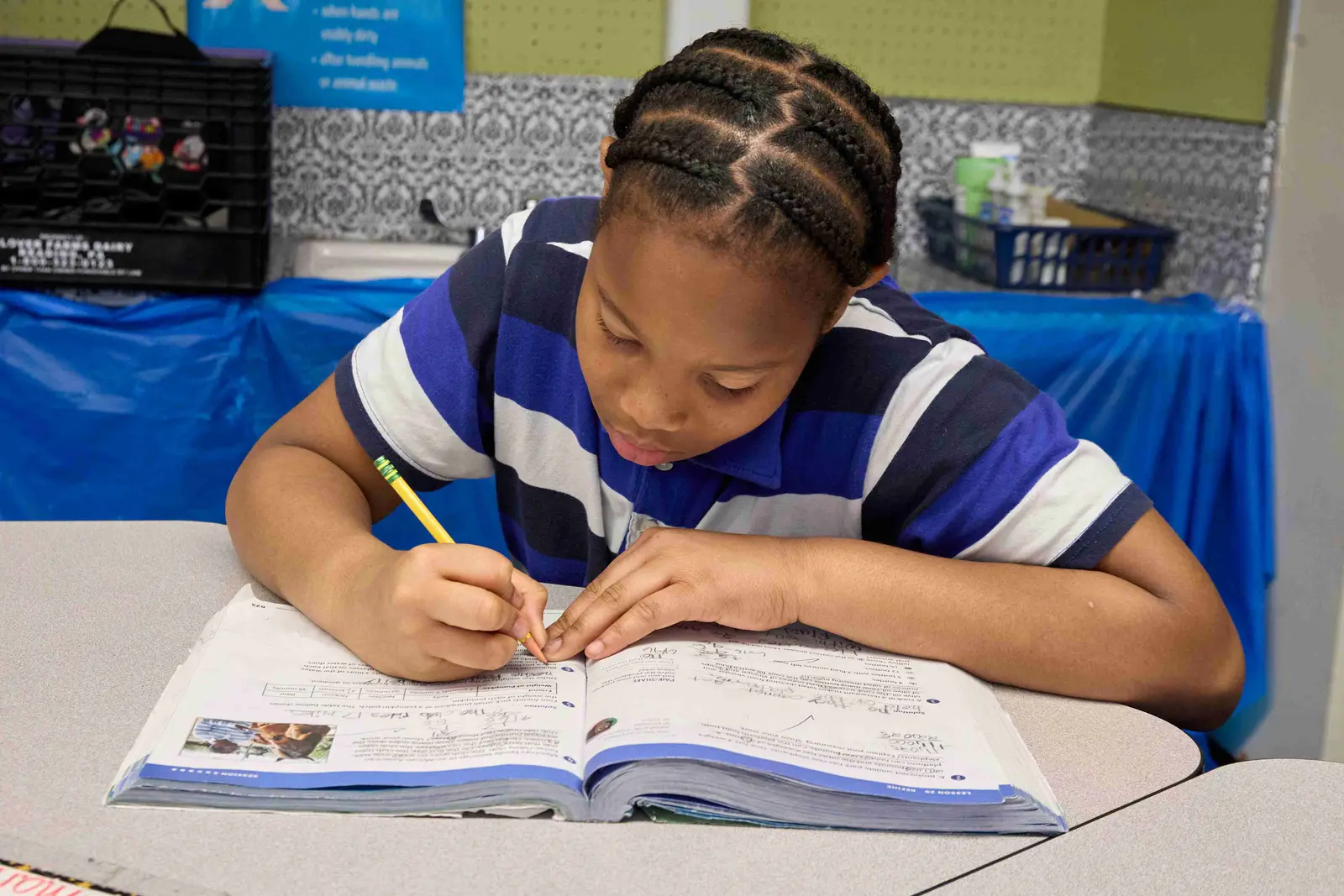 Student writing in a textbook with a pencil at her desk