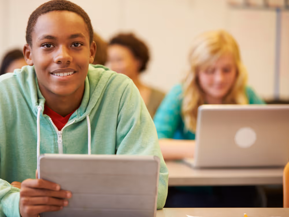 student smiling holding tablet in class