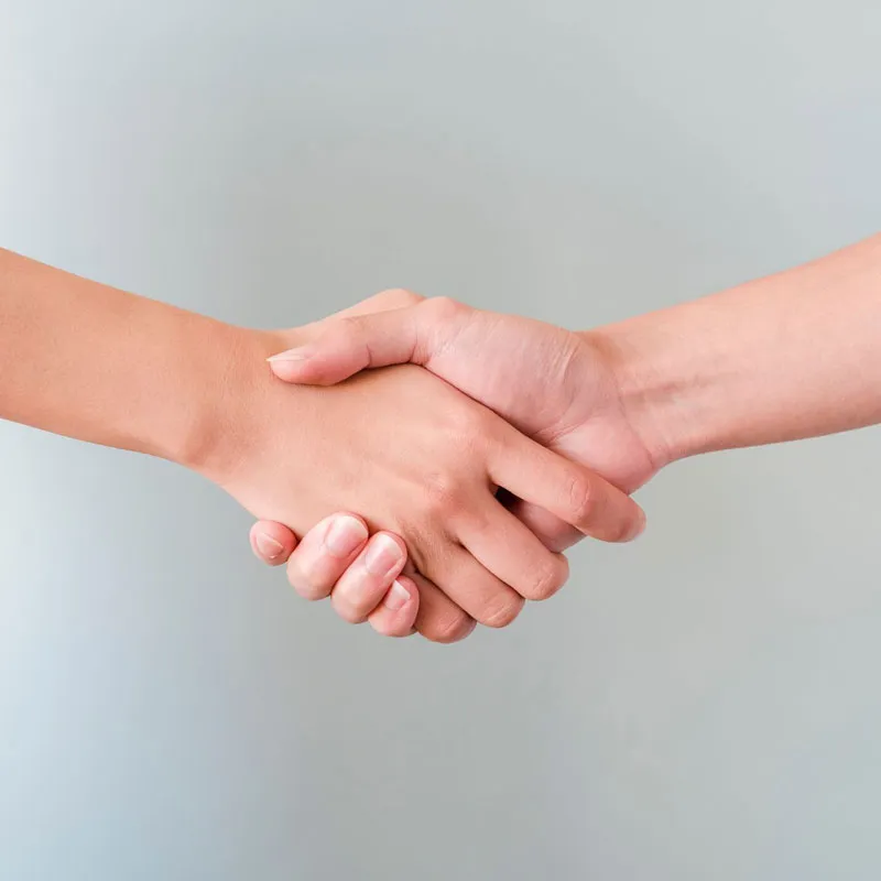 Close-up of two hands shaking in agreement against a plain light gray background.