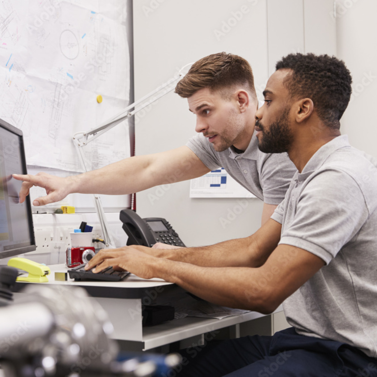 2 men at a desk sharing a computer screen, one is pointing to the screen