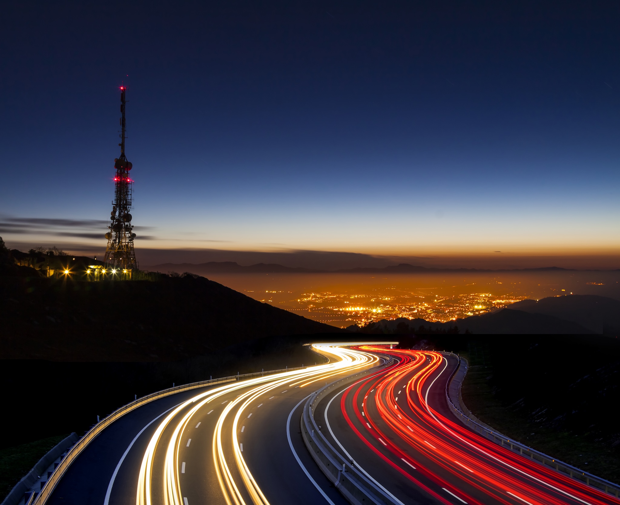 Timelapse photo at dusk showing highway traffic and a telephone tower