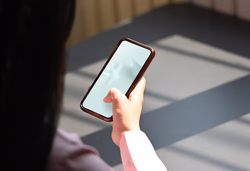 A person's hand holding a smartphone with a blank screen, showcasing its display with natural light casting shadows across it.