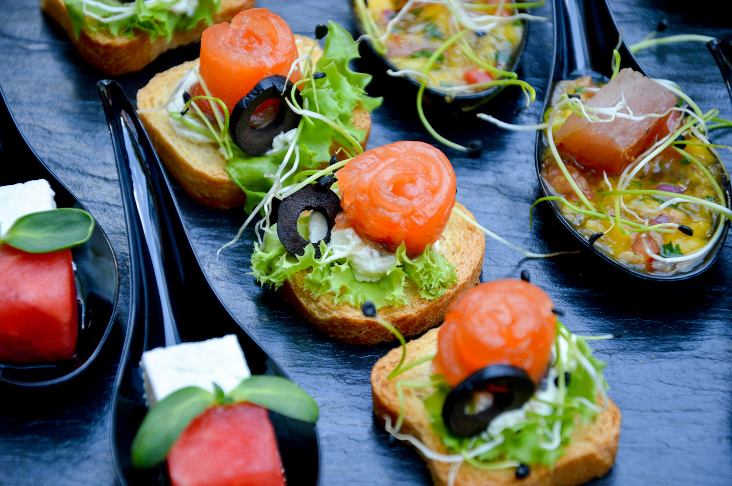 Elegant catering appetizers with smoked salmon, vegetables, and fresh garnish served on bread and spoons.