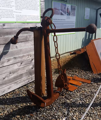 A large metal anchor sitting on top of a gravel field.