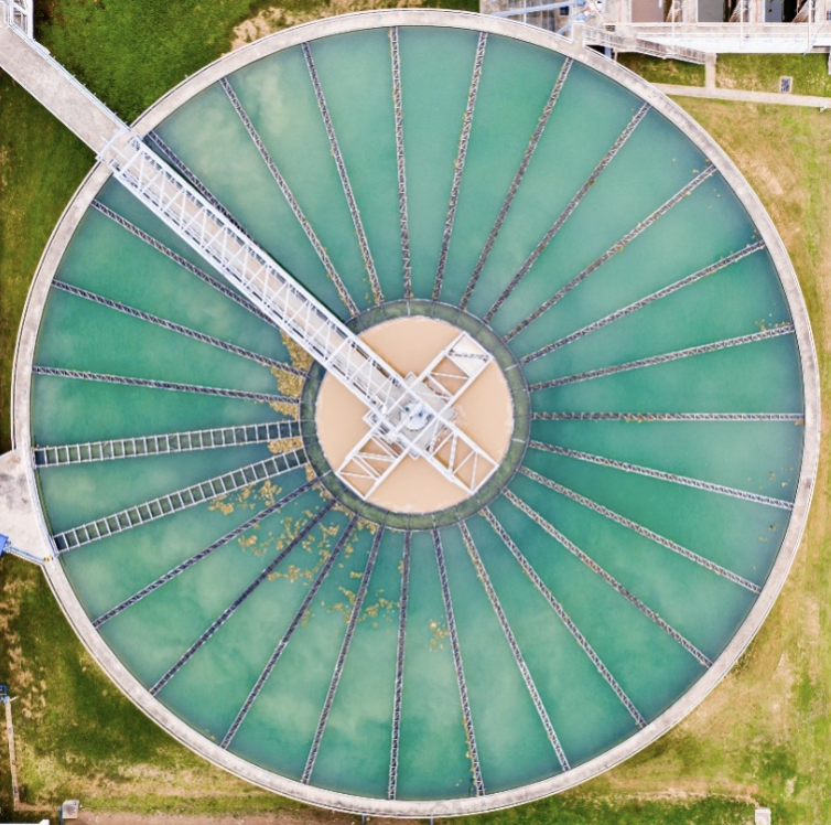 Aerial view of a circular clarifier with visible algae and biofilm on the surface