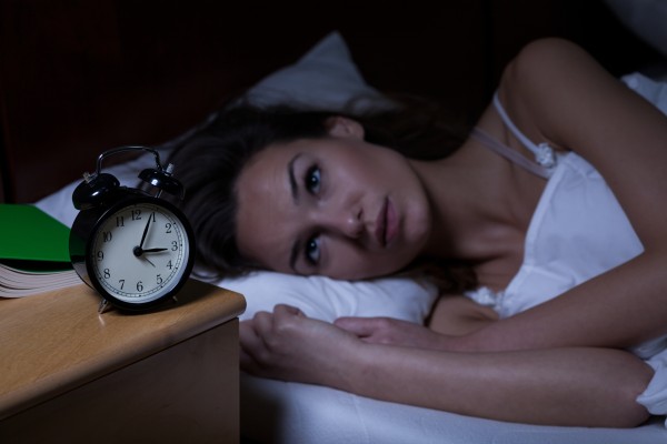 A woman lays awake at night staring at the clock