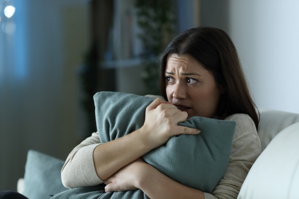 A woman sits clutching a pillow looking concerned