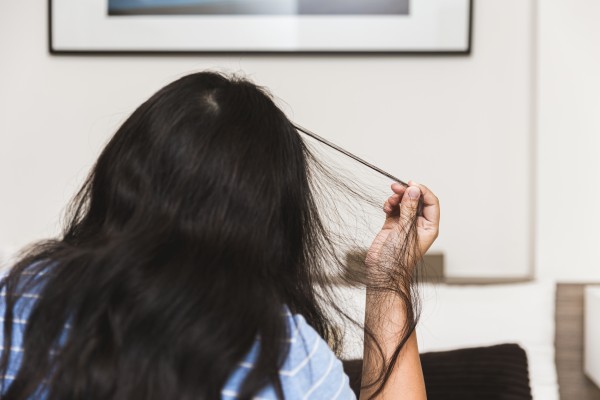 A woman sits facing away from the camera, pulling at her hair