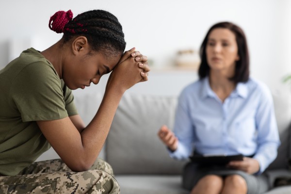 A military veteran sits with her hands clasped and her head low