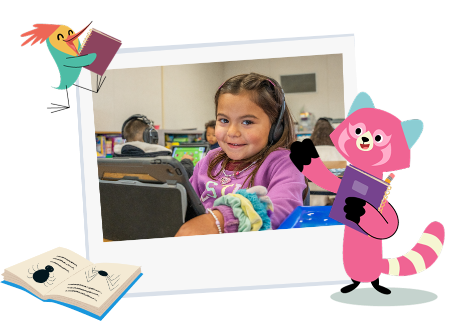 Young girl smiling behind the computer while using a free Khan Kids in a classroom setting.