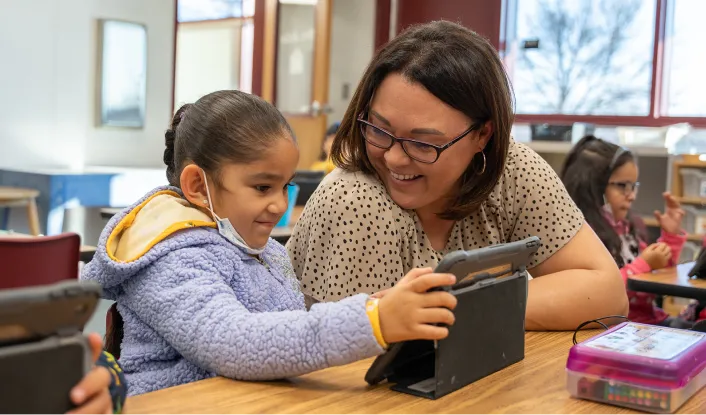 Smiling teacher helping a young student build english language skills with Khan Academy Kids.