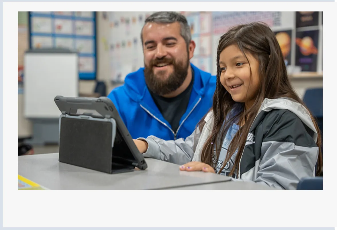 Teacher and young student using Khan Academy Kids on tablet in classroom setting. 