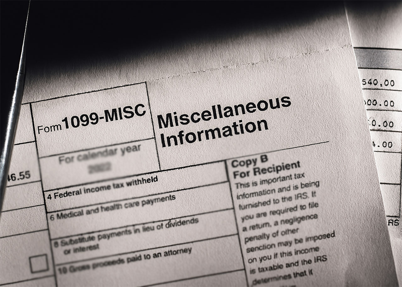 Close-up of a 1099-MISC tax form labeled “Miscellaneous Information,” partially covered by another document, under dramatic lighting.