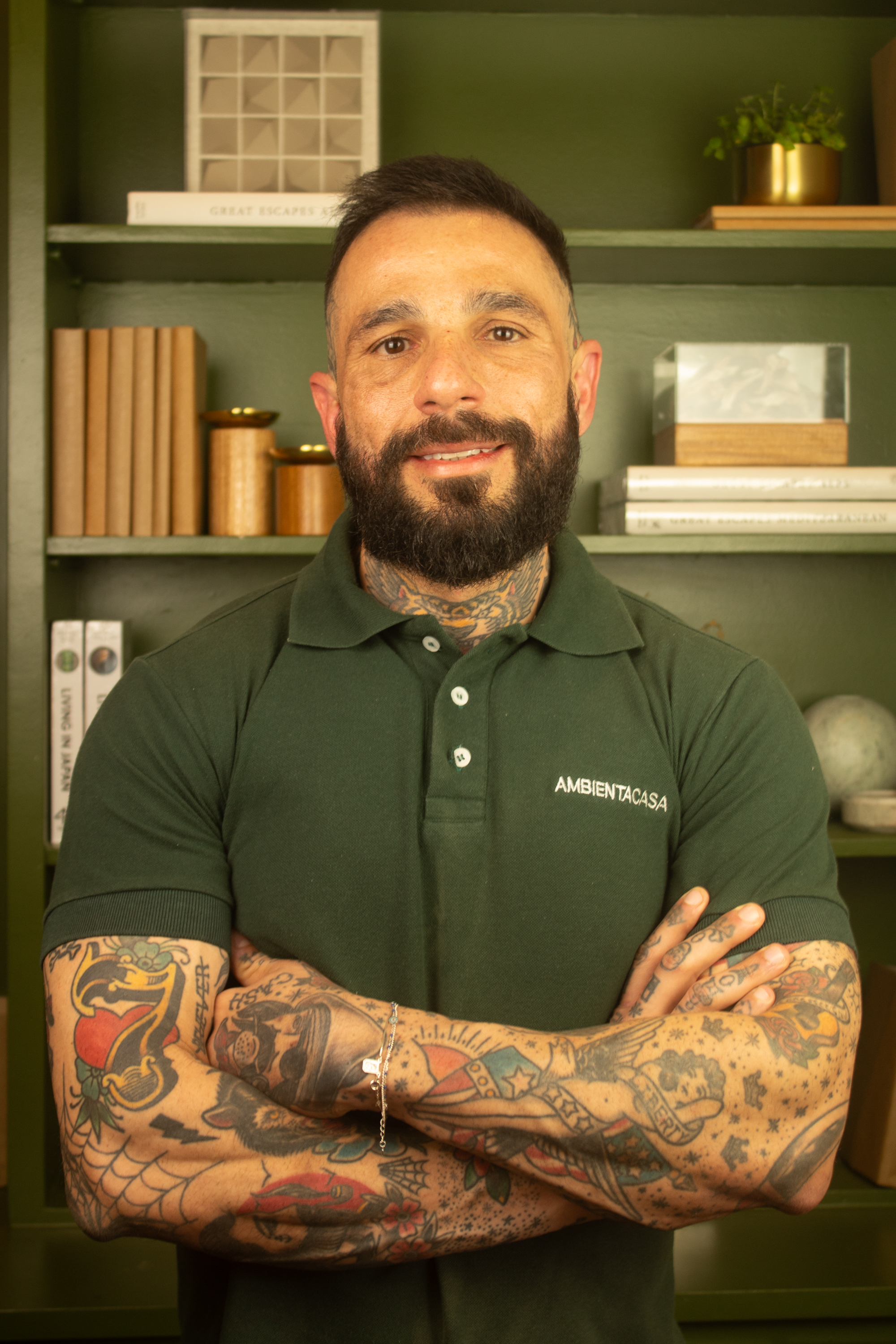 Luis Artur, sócio da Ambienta Casa, com uma camisa polo verde e uma estante com livros e decorações atrás.