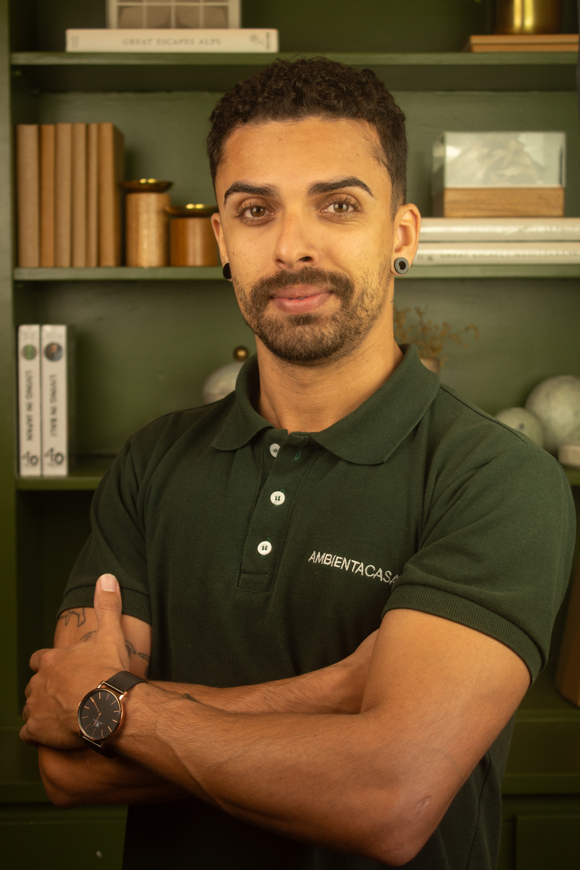 Samuel Furlan, colaborador da Ambienta Casa, com uma camisa polo verde e uma estante com livros e decorações atrás.