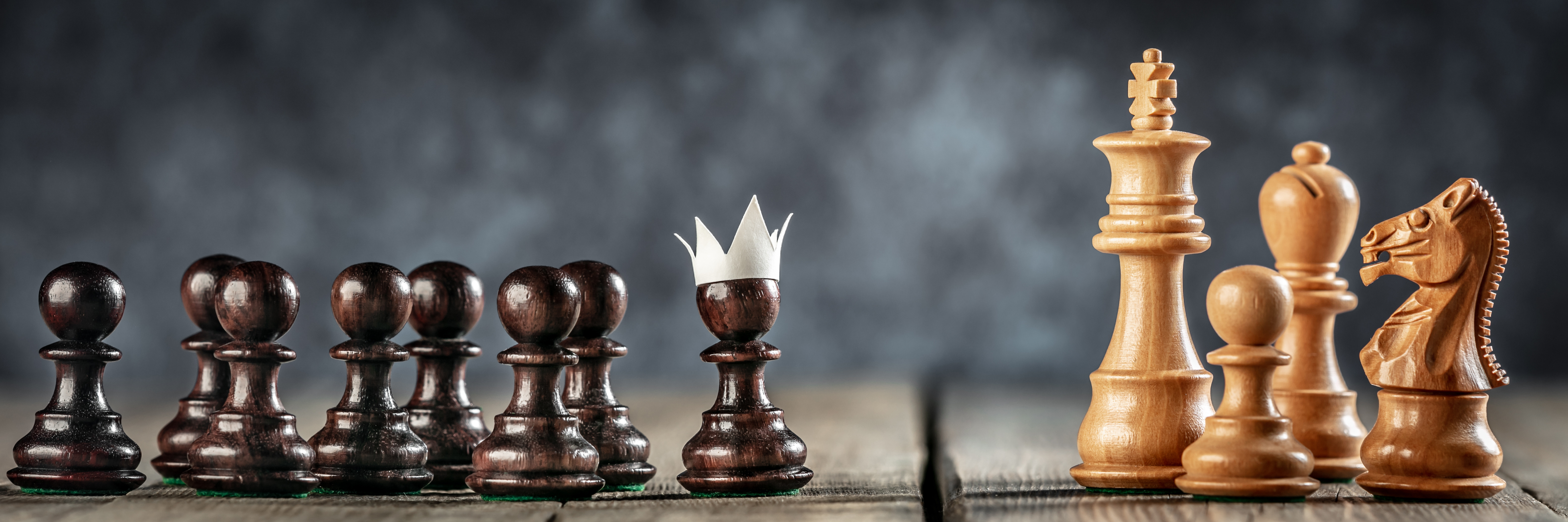 Chess pawns lined up with one pawn wearing a paper crown, facing larger chess pieces — symbolizing leadership development, potential, and growth at AWL Partners in Toronto.
