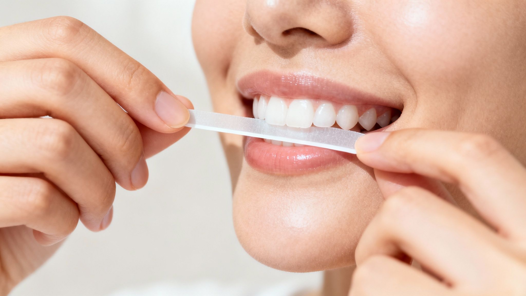 Close-up of a person applying a teeth whitening strip to their bright white upper teeth.
