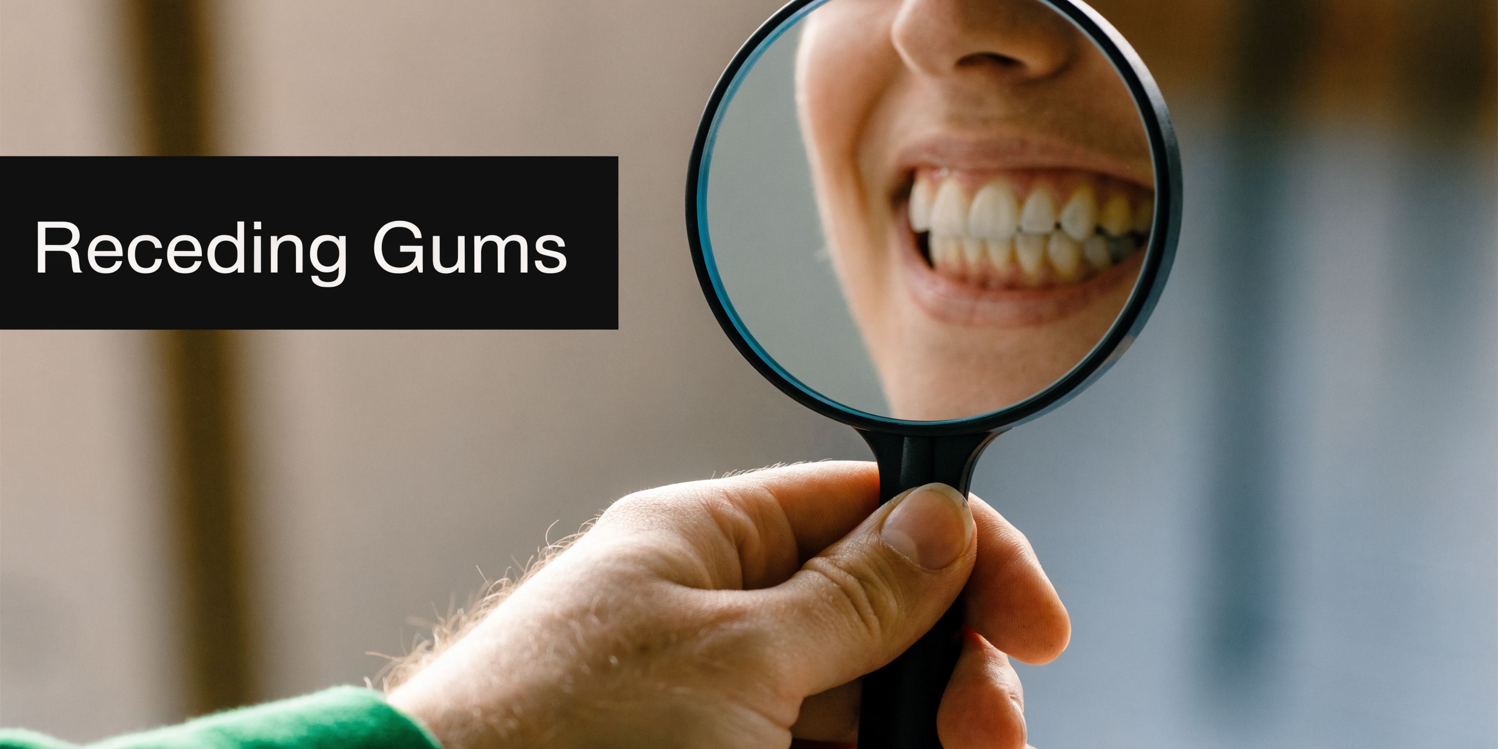 A magnifying glass held in a person's hand focusing on a smile that shows signs of receding gums.