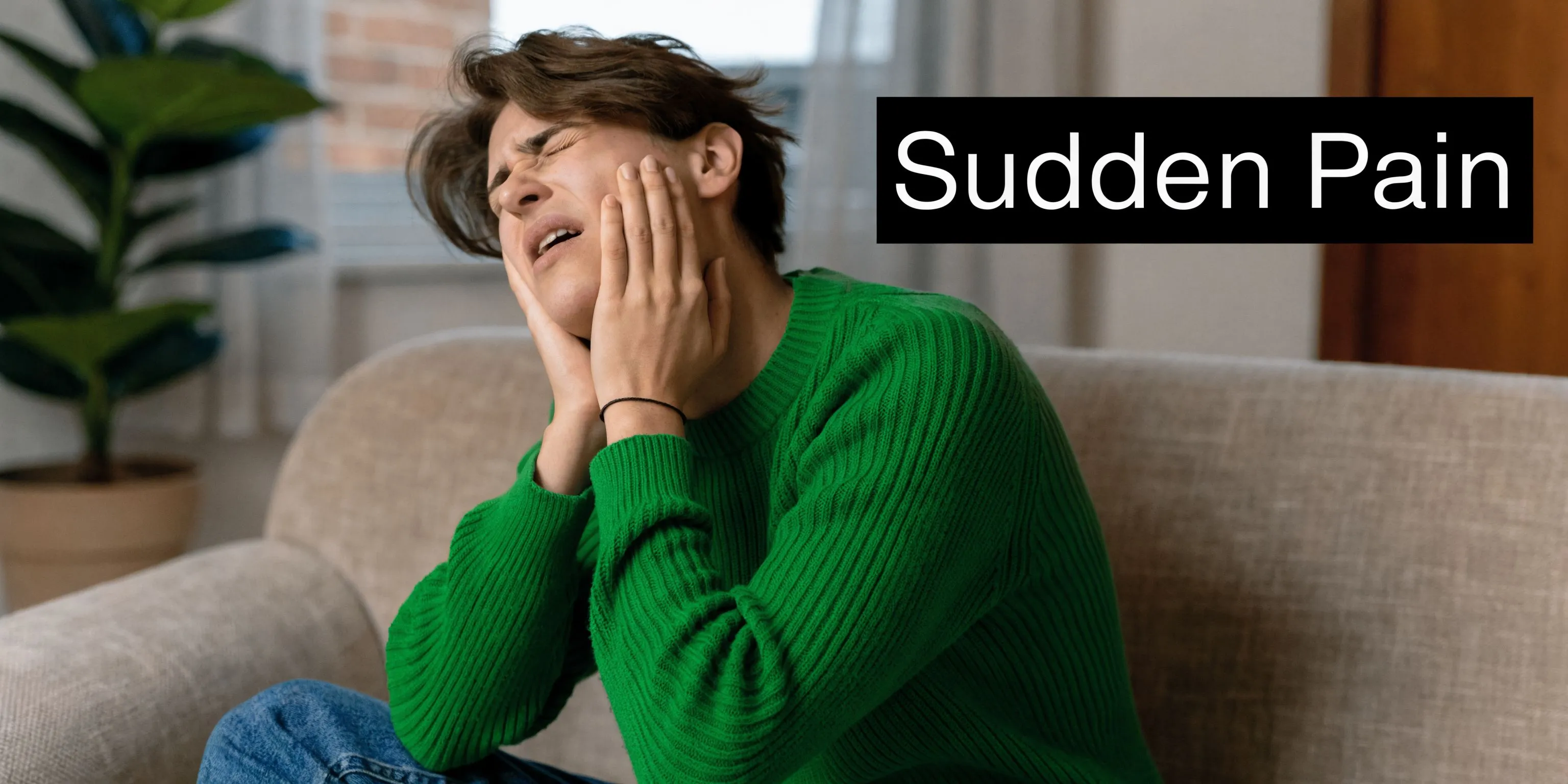A person in a green sweater holding their jaw in sudden pain while sitting on a couch.