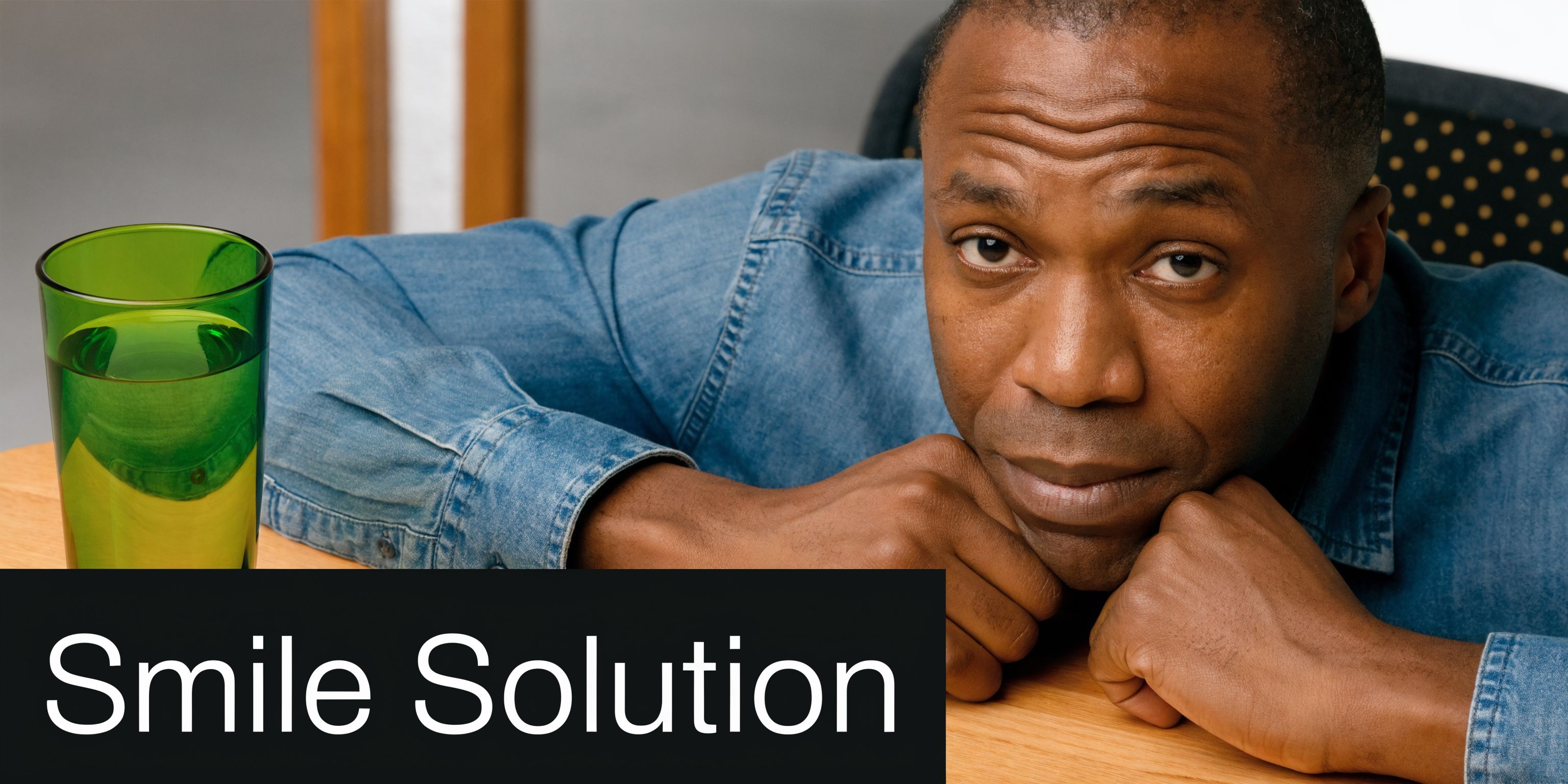 A pensive man resting his chin on his hands next to a glass of water, contemplating dental care.