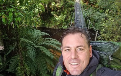 A hiker on a wire bridge over a river in the jungle