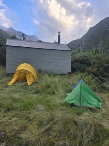 2 hiking tents pitched next to a cabin in the mountains