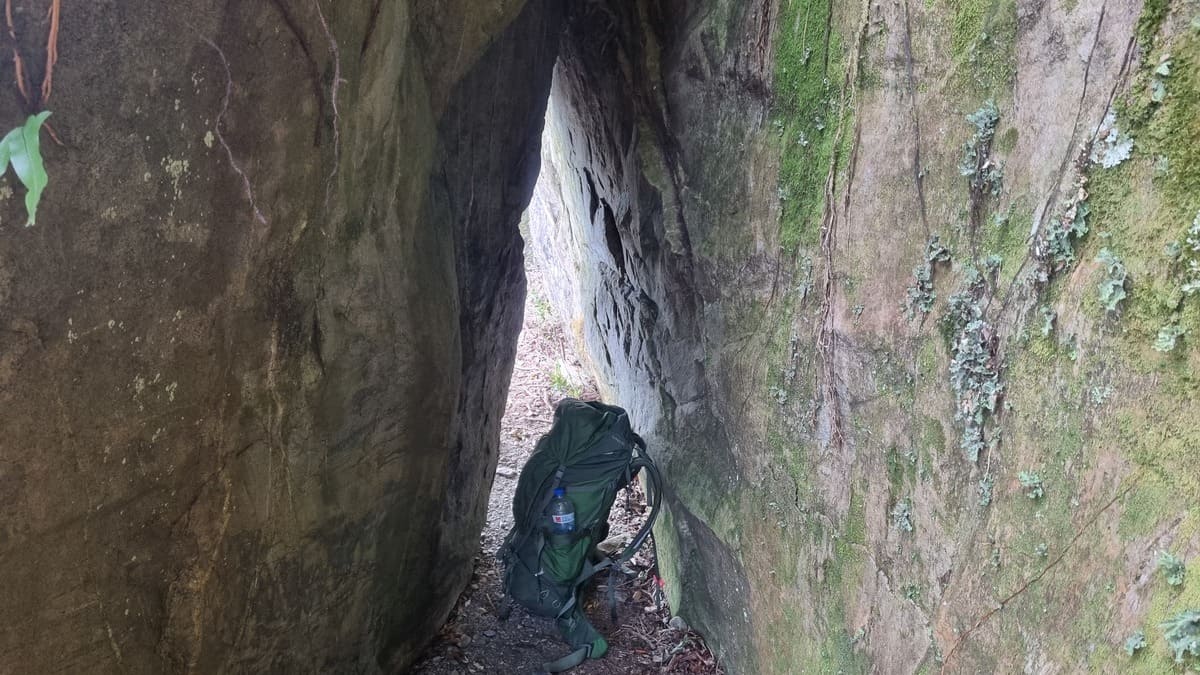 A hiking pack sits on the trail in a narrow crack in a rock wall