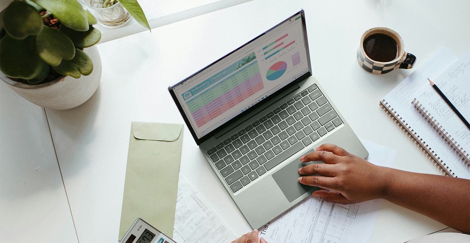Business owner working with spreadsheets on a laptop alongside financial papers and a calculator, showing the challenges of DIY bookkeeping.