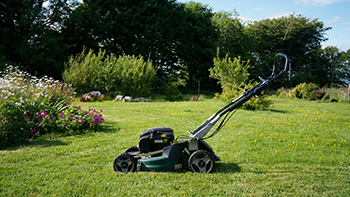 A lawn mower parked on a freshly cut lawn with trees and flowerbeds in the background, representing home and field service work in Forest Lake.